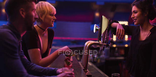 Camarero interactuando con pareja en el mostrador en el bar - foto de stock