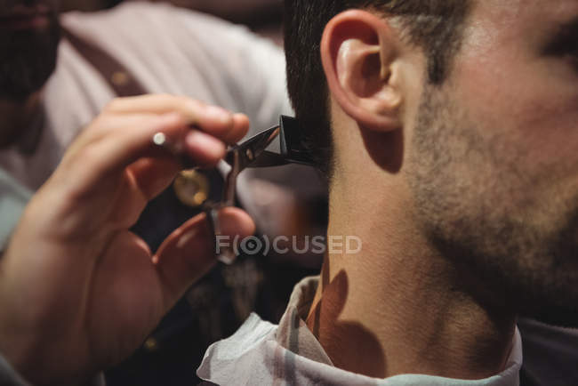 Close-up de homem recebendo cabelo aparado por cabeleireiro com tesoura na barbearia — Fotografia de Stock