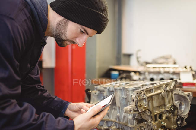 Mécanicien utilisant tablette numérique sur les pièces de voiture dans le garage de réparation — Photo de stock