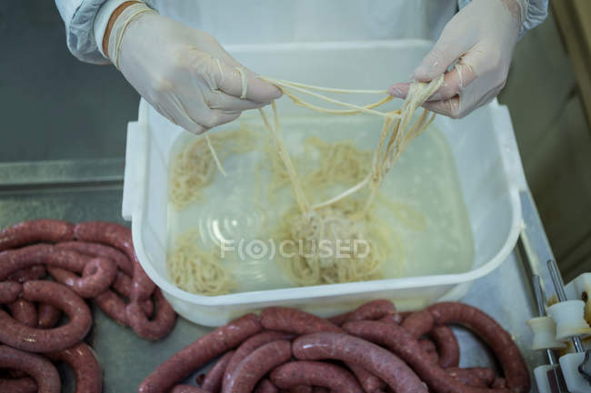 Mid-section of butcher processing sausages in meat factory — Stock Photo