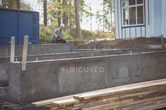 Fundação de concreto e tábuas de madeira no canteiro de obras, homem trabalhando no fundo — Fotografia de Stock