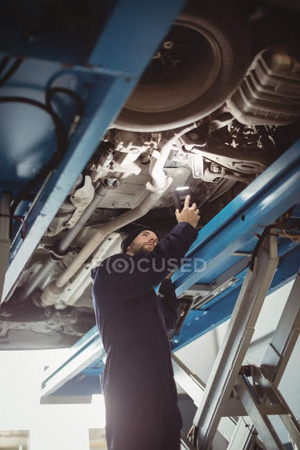 Mécanicien examinant une voiture avec lampe de poche dans le garage de réparation — Photo de stock