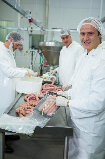 Macellai imballaggio e lavorazione salsicce crude in fabbrica di carne — Foto stock
