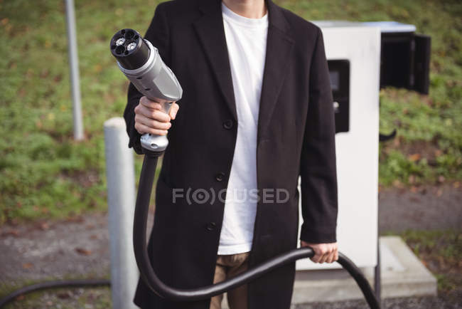 Mid section of man holding car charger at electric vehicle charging station — Stock Photo