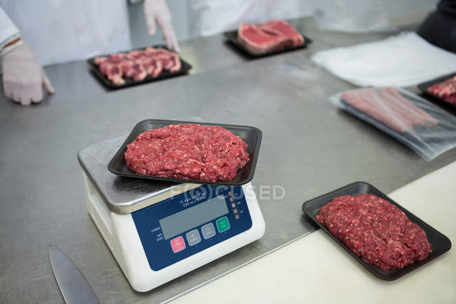 Butcher weighing packages of minced meat at meat factory — Stock Photo