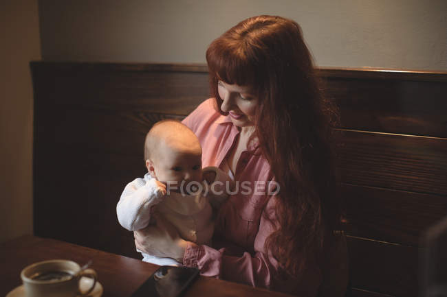 Mãe segurando pequeno bebê nos braços na mesa de café — Fotografia de Stock