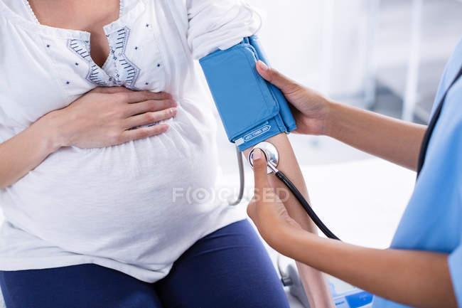 Середній відділ лікаря, який перевіряє артеріальний тиск вагітної жінки в лікарні — стокове фото