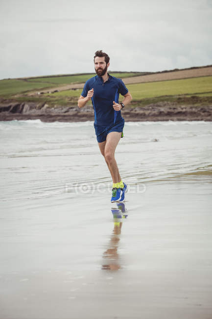 Atleta bonito correndo ao longo da praia arenosa — Fotografia de Stock