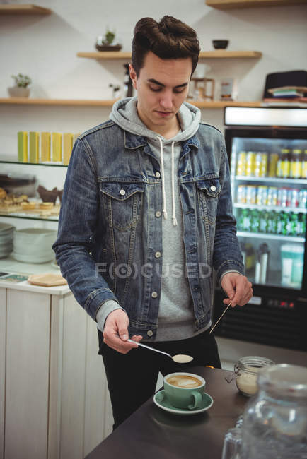 Man holding spoon over a coffee cup in coffee shop — Stock Photo