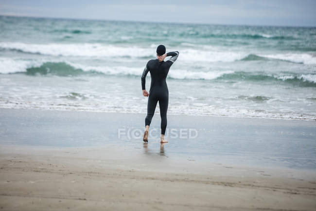 Vista trasera del atleta en traje de neopreno de pie en la playa - foto de stock