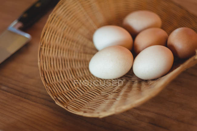 Яйца в плетеной корзине на деревянном столе на кухне — стоковое фото