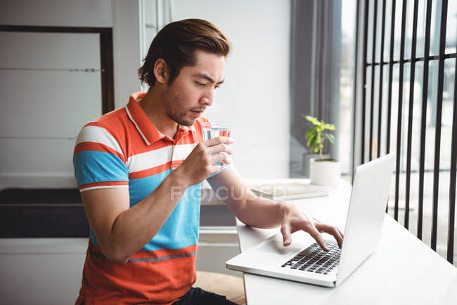 Homem usando laptop enquanto bebe água no café — Fotografia de Stock