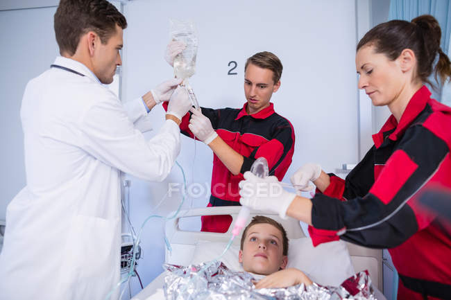 Médico y paramédicos examinando a un paciente en la sala de emergencias del hospital - foto de stock