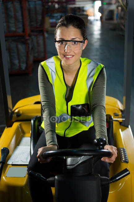 Retrato de uma jovem trabalhadora que conduz empilhadeira no armazém — Fotografia de Stock