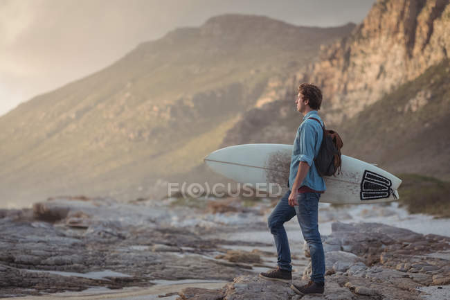 Side view of a man carrying a surfboard standing by sea at dusk — Stock Photo