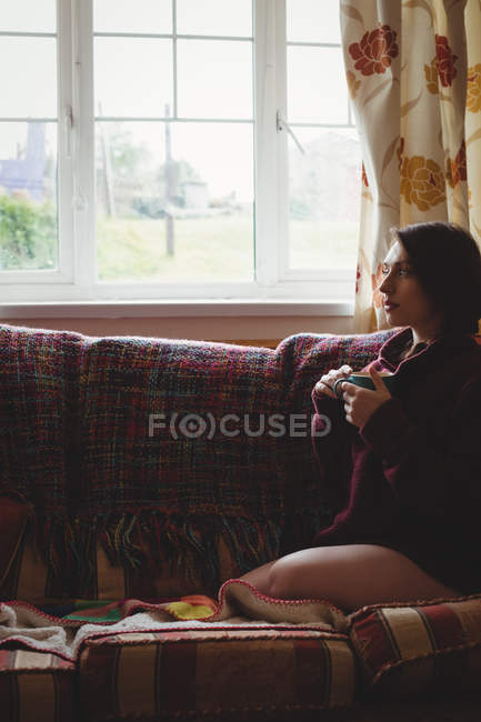Mulher pensativo sentado e segurando uma xícara de café em casa — Fotografia de Stock