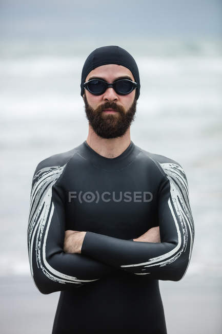 Athlete in wet suit standing with his arms crossed on beach — Stock Photo