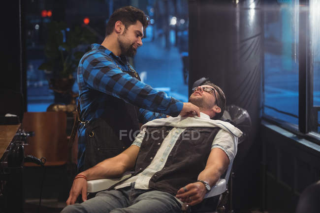 Peluquero poniendo toalla sobre el cliente en la peluquería - foto de stock