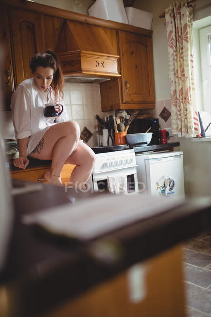 Femme réfléchie assise et prenant un café dans la cuisine à la maison — Photo de stock