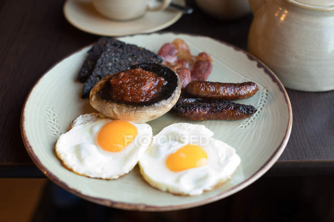 Plate of english breakfast with eggs and sausages on table — Stock Photo