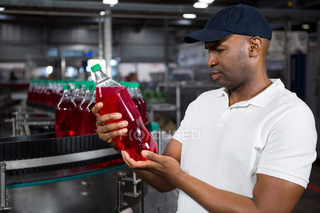 Jovem trabalhador masculino inspecionando garrafa de suco na fábrica — Fotografia de Stock