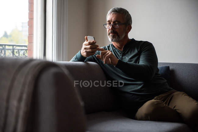 Hombre usando el teléfono móvil en la sala de estar en casa - foto de stock