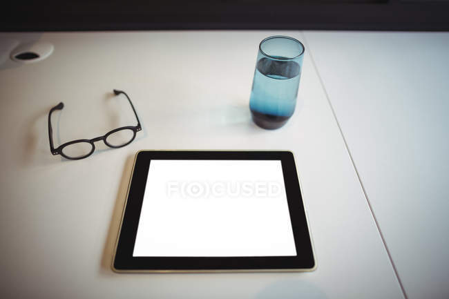 Tableta digital con espectáculo y vaso de agua en el escritorio de la oficina en la oficina - foto de stock