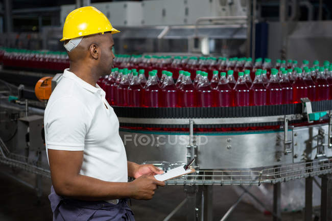 Vista lateral del trabajador masculino inspeccionando botellas en fábrica de jugo - foto de stock