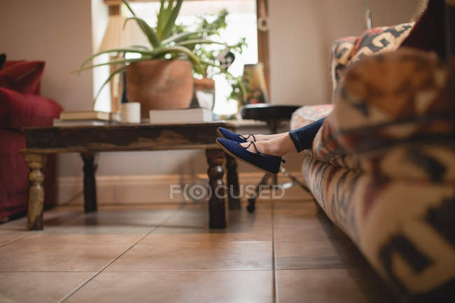 Jambes de fille assise sur le canapé dans le salon à la maison — Photo de stock