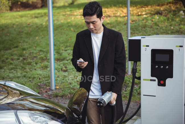 Mann benutzt Handy beim Aufladen von Auto an Elektroauto-Ladestation — Stockfoto