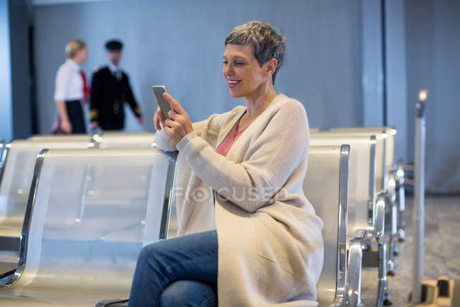 Donna sorridente che utilizza il telefono cellulare in sala d'attesa al terminal dell'aeroporto — Foto stock