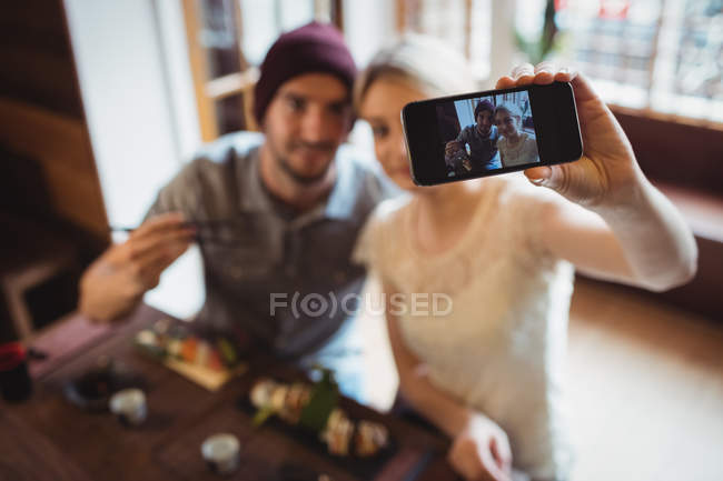 Пара, делающая селфи во время еды суши в ресторане — стоковое фото