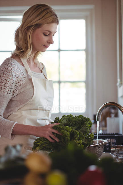 Beautiful woman washing broccoli under sink in kitchen at home — Stock Photo