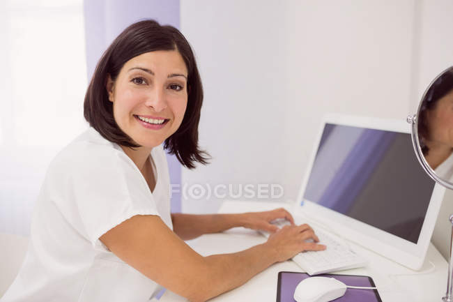 Sonriente médico femenino usando PC de escritorio en la clínica - foto de stock