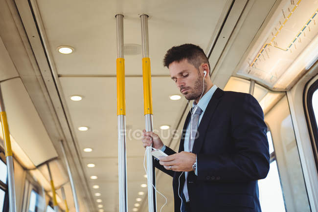 Empresario escuchando música y usando el teléfono móvil en el tren - foto de stock