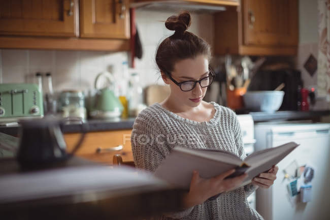 Woman reading book in kitchen at home — Stock Photo