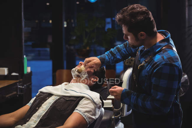 Peluquería aplicar crema en la barba del cliente en la peluquería - foto de stock