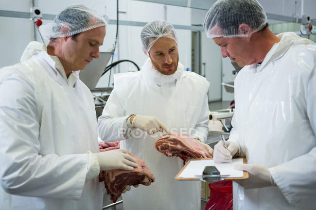 Carniceros manteniendo registros en el portapapeles en la fábrica de carne - foto de stock