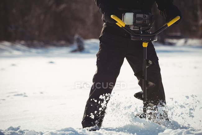Partie médiane du forage d'un pêcheur sur glace dans la neige — Photo de stock