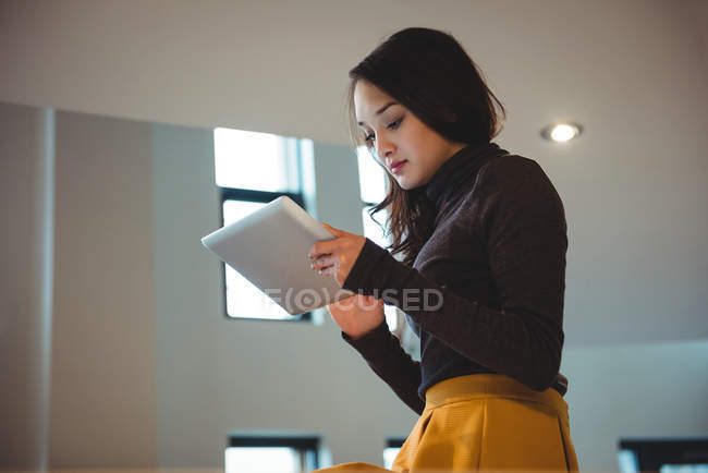 Femme assise sur le plan de travail de la cuisine en utilisant une tablette numérique à la maison — Photo de stock