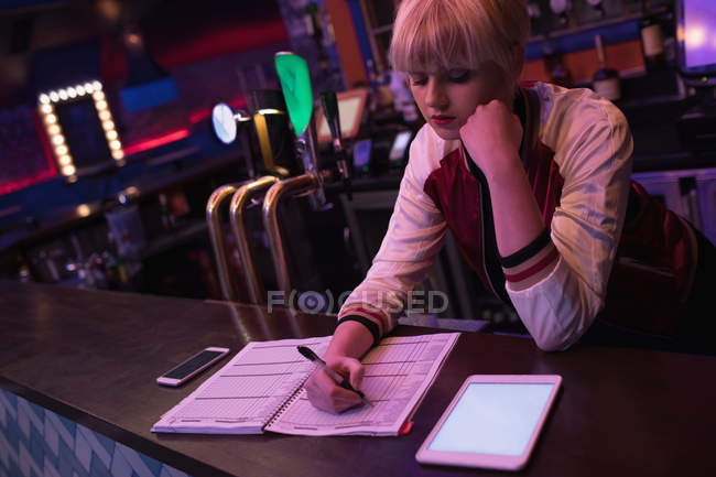 Barman femelle utilisant une tablette numérique tout en conservant les dossiers au comptoir dans le bar — Photo de stock