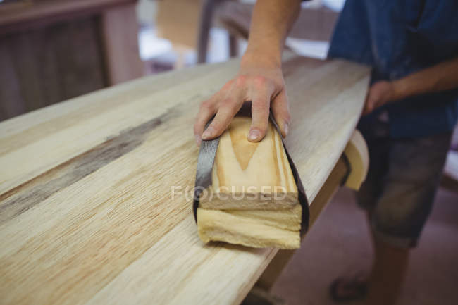 Primo piano dell'uomo che utilizza la levigatrice su tavola da surf in officina — Foto stock