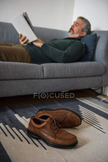 Mann liest Buch zu Hause im Wohnzimmer — Stockfoto