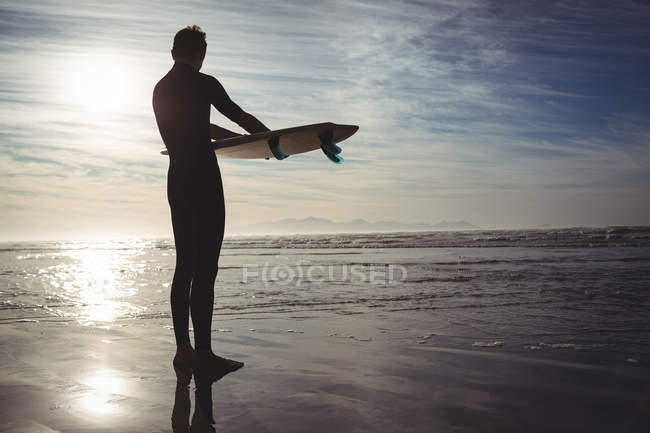 Силуэт серфера, стоящего с доской для серфинга на пляже — стоковое фото