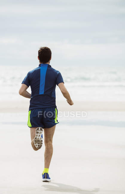 Vue arrière de l'athlète qui court sur une plage mouillée — Photo de stock