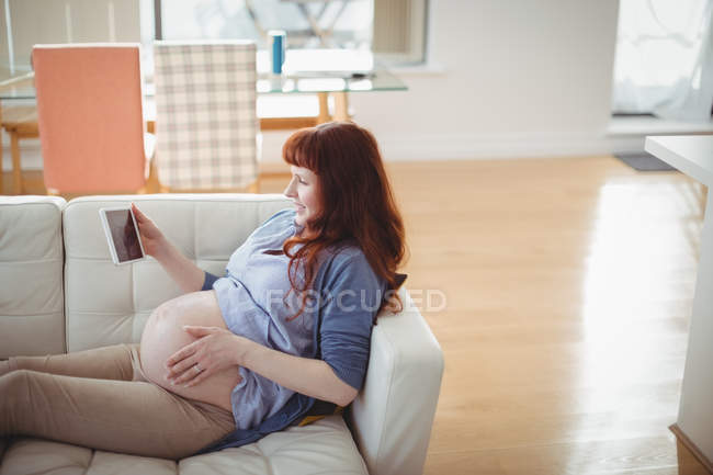 Вагітна жінка дивиться на сонографію на цифровому столі у вітальні — стокове фото