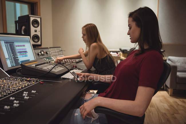 Ingenieros de audio usando un teléfono móvil conectado al mezclador de sonido en un estudio de grabación - foto de stock