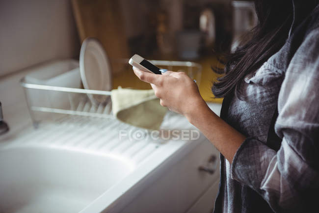 Seção média de mulher usando telefone celular na cozinha — Fotografia de Stock