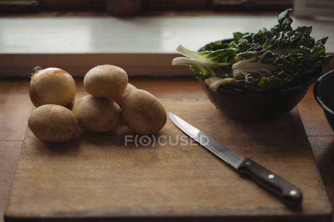 Primer plano de Patatas, cebolla y lechuga sobre tabla de cortar con cuchillo - foto de stock
