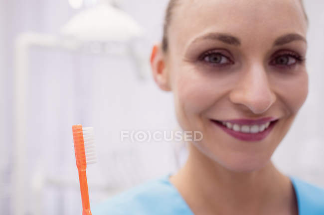 Retrato de dentista feminina segurando escova de dentes na clínica odontológica — Fotografia de Stock